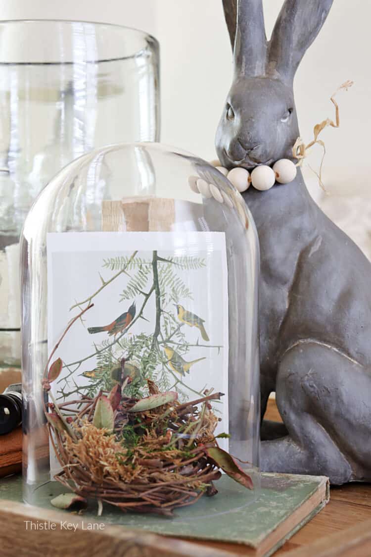 Rabbit figurine and a cloche with a bird nest. Three Spring Ottoman Or Coffee Table Vignettes.