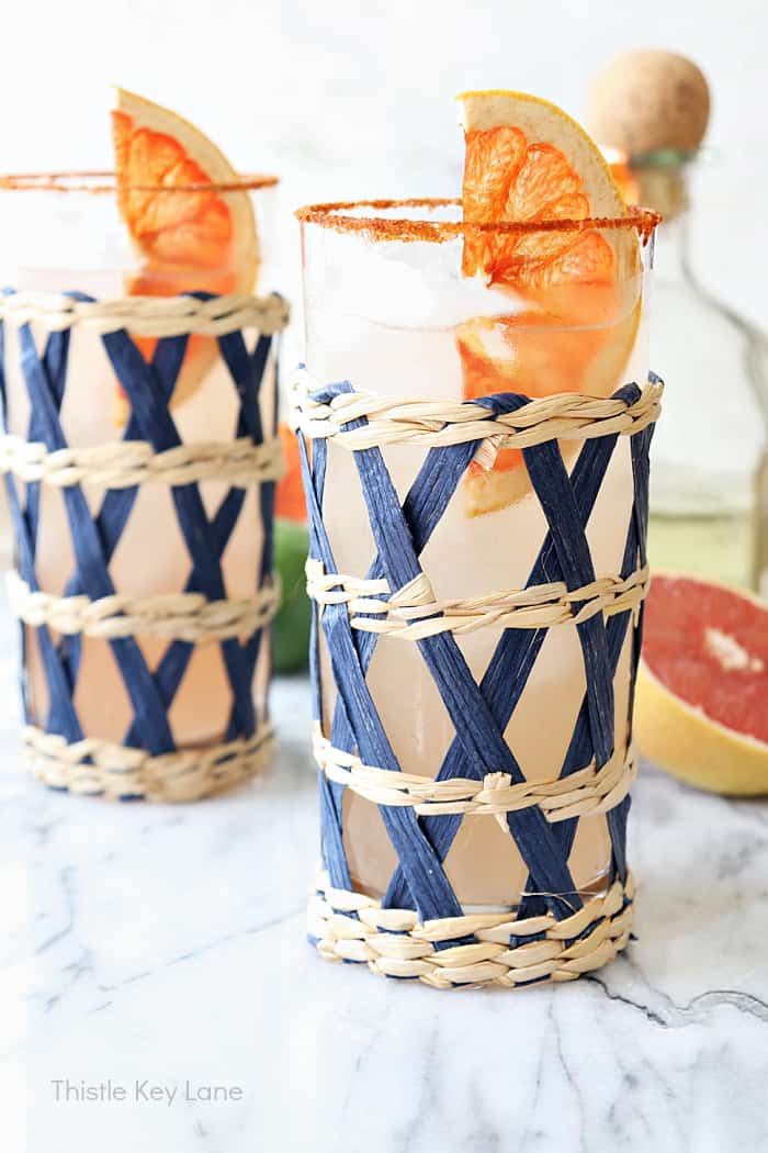 addison: A Paloma cocktail with large clear ice cubes in a tall collins  glass garnished with a grapefruit peel on a white marble counter top