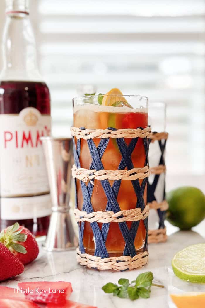 Tall drink in wicker wrapped glass. Pimm's Cup Cocktail Recipe.