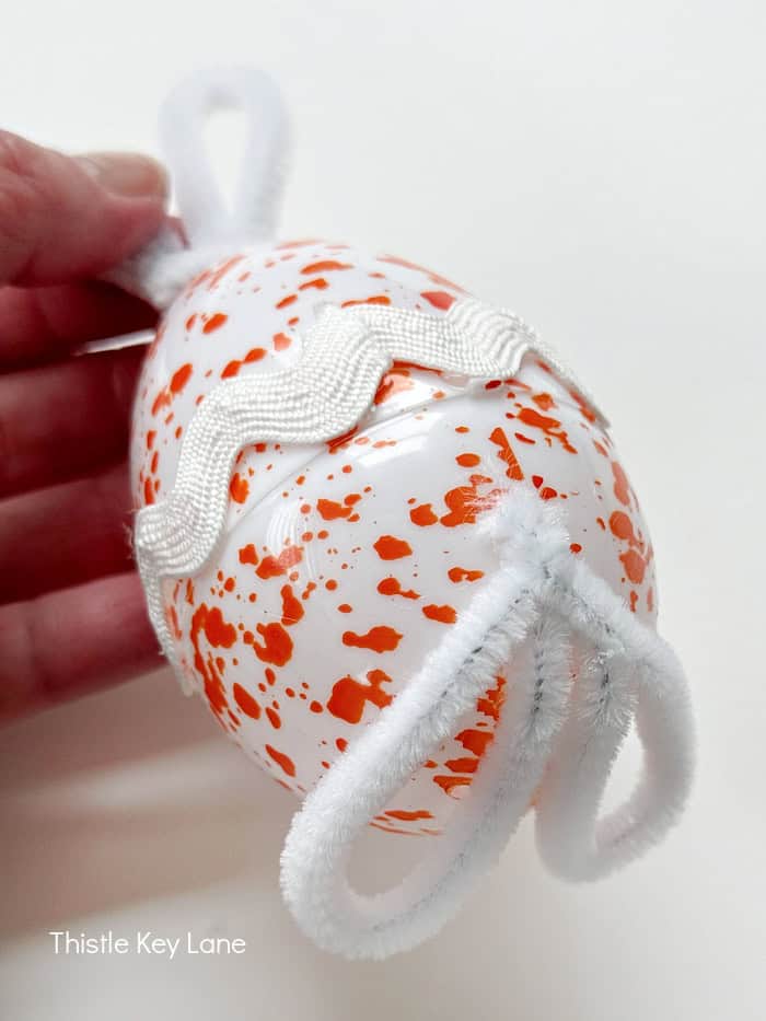Hot glue pipe cleaner feet to the egg.