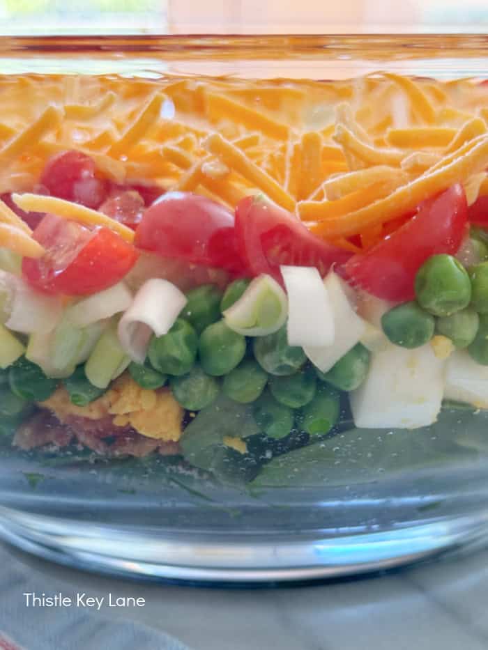 Side of glass bowl showing salad layers. Green Pea Layered Salad Recipe.