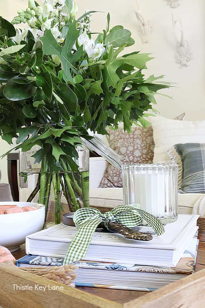 Candle, magnifying glass, stack of books, fresh arrangement. Summer Fresh Ottoman Styling.