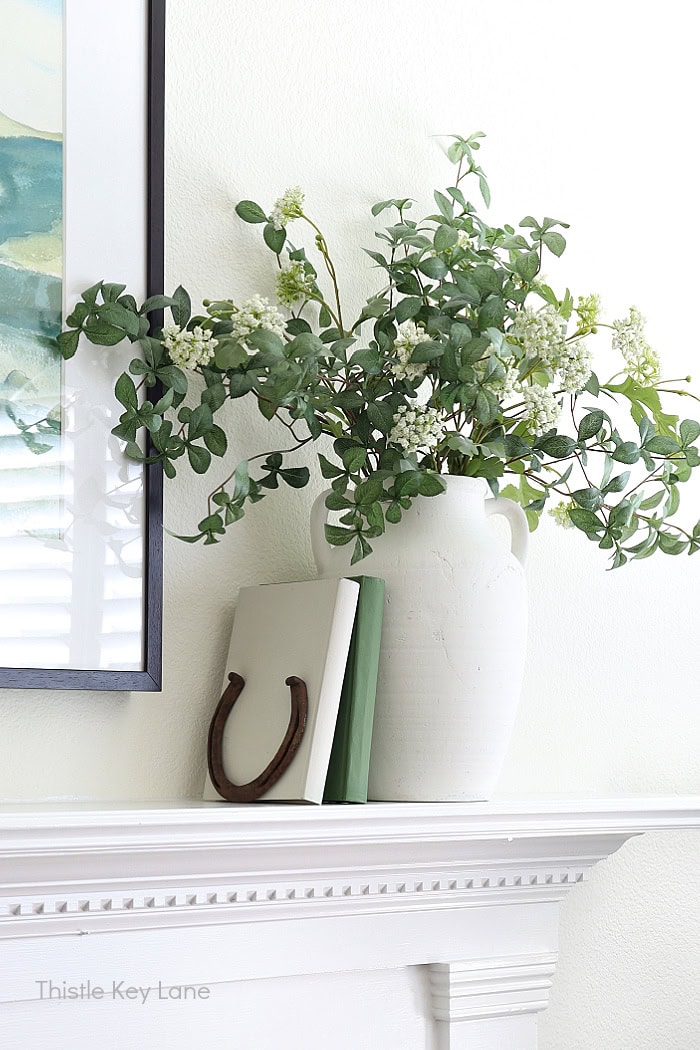 White vase with faux flowers, books and horseshoe. Summer Family Room Cottage Styling.
