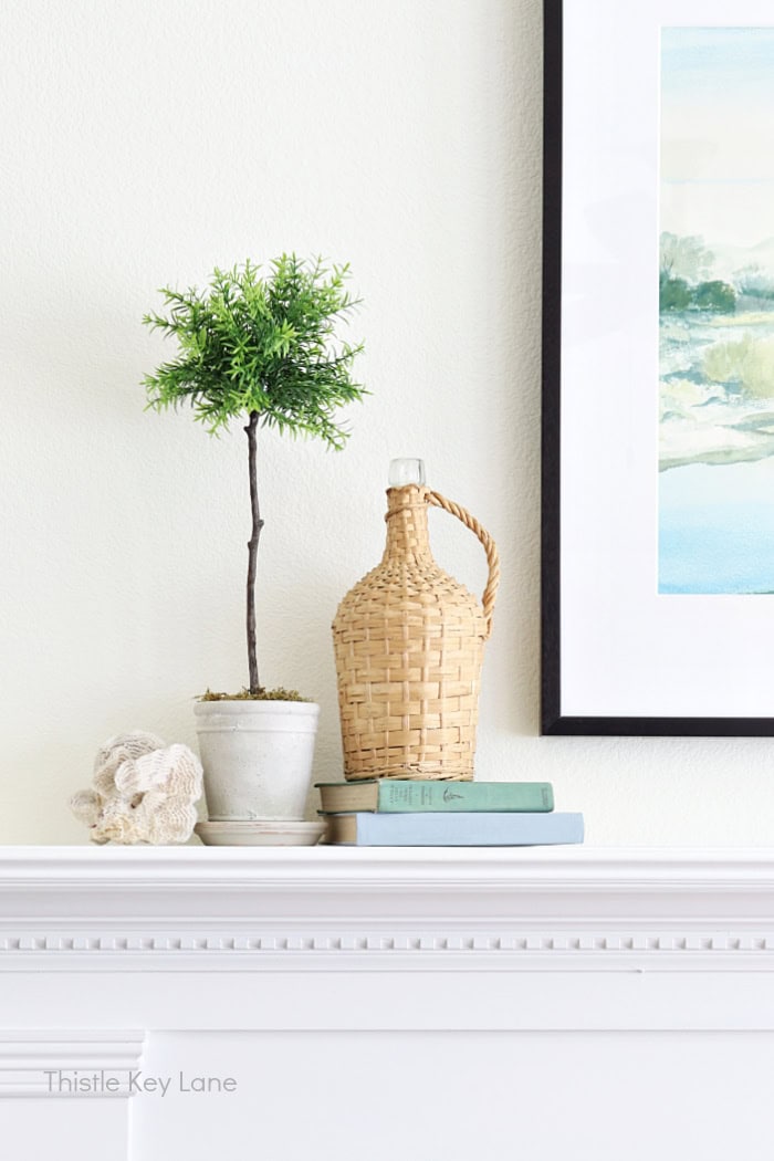 Coral, topiary, vintage wine bottle and books on mantel. Summer Family Room Cottage Styling.