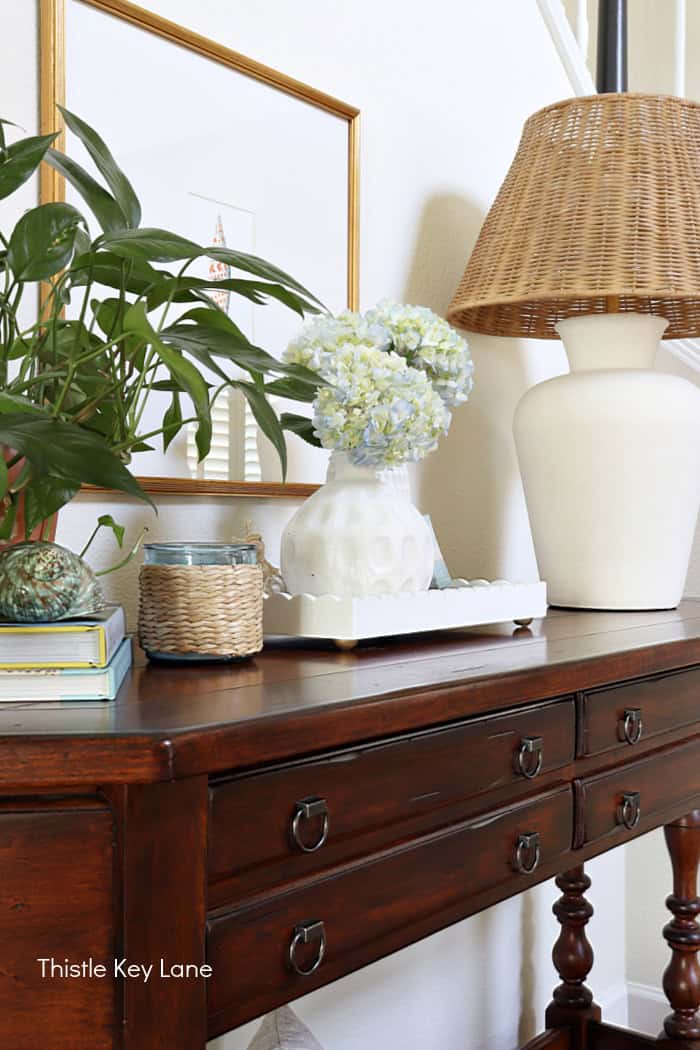 Plant, books, rattan shade and lamp. Coastal Cottage Entry Table.