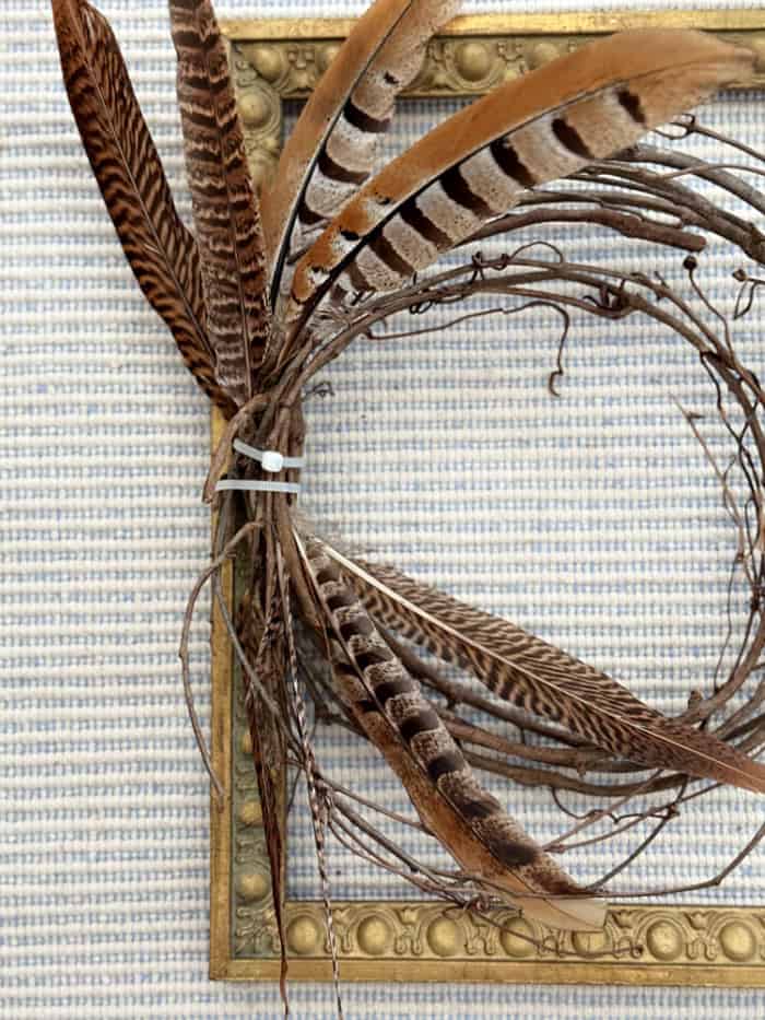 Adding feathers to the grapevine wreath. DIY Vintage Frame Wreath With Feathers.