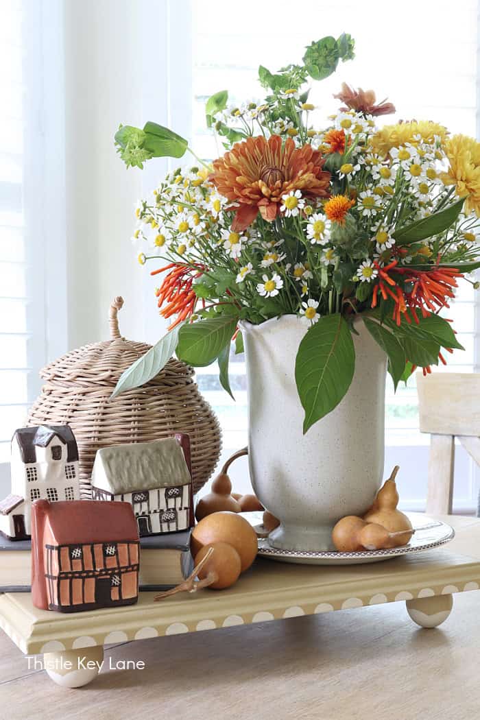 Vase of flowers, wicker pumpkin, tiny houses. Autumn Vintage Cottage Vignette.