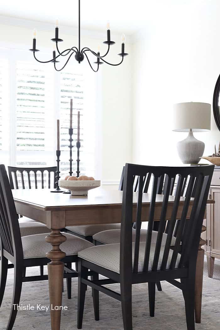 Maple dining table and dark stained chairs with cream cushions, black chandelier, and white walls. Dining Room Update And Fall Styling.