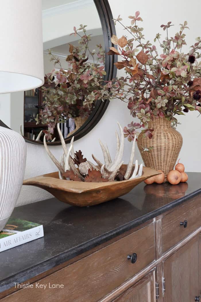 Wood dough bowl with deer sheds, gourds and wicker vase with fall stems on a buffet table. Dining Room Update And Fall Styling.