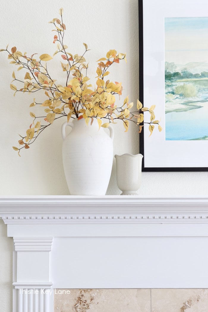 Elegant white vase with yellow and orange leaves on a decorative mantel. Cozy Autumn Family Room Decor.