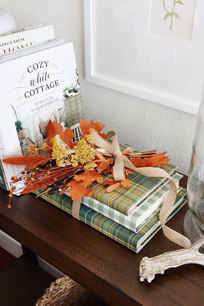 Orange leaves tied with ribbon on top of a plaid book. Fall Dried Florals Book Vignette.
