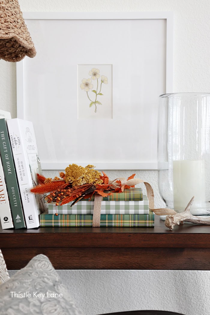 Books on a table with artwork and a candle. Fall Dried Florals Book Vignette.