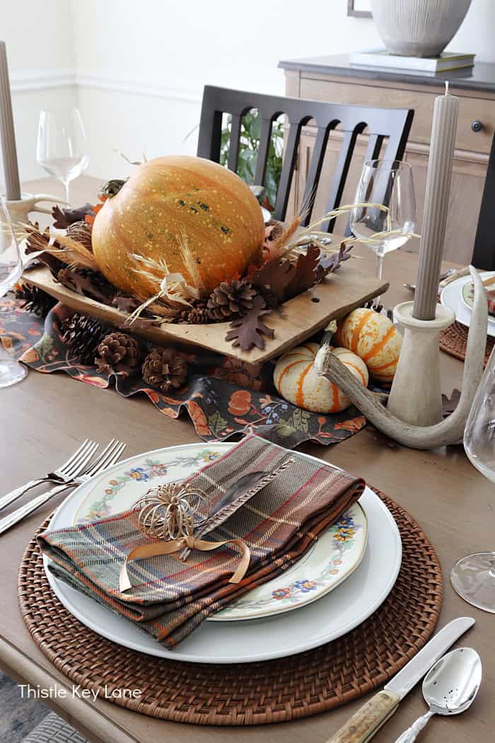 White dishes and plaid napkins with a feather. Rustic Thanksgiving Pumpkin Centerpiece And Tablescape.