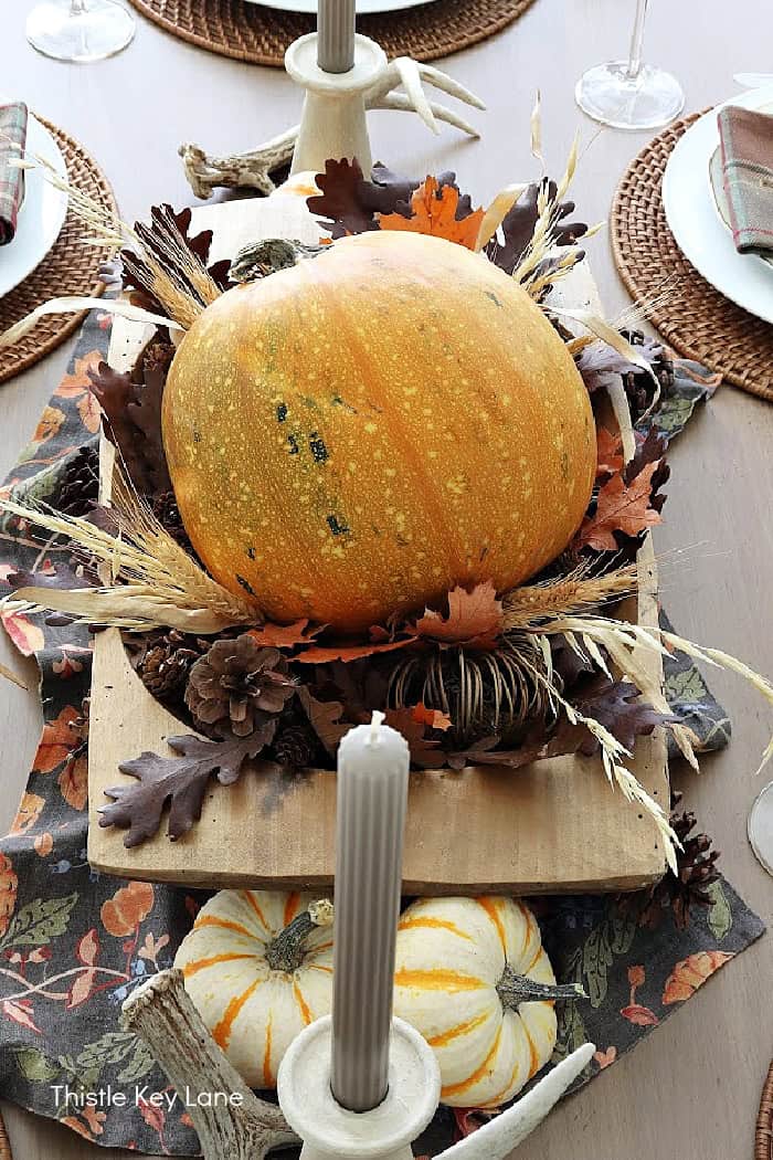 View of pumpkin centerpiece with pinecones, candles, leaves.