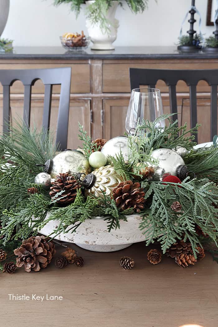 Centerpiece with glass ornaments, pinecones and greenery. Holiday Dining Room With Festive Greenery.