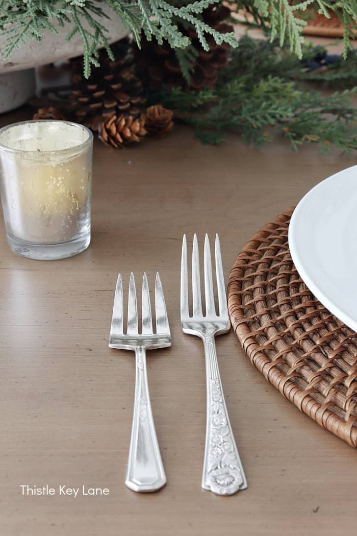 Vintage silverware next to a place setting. Holiday Dining Room With Festive Greenery.