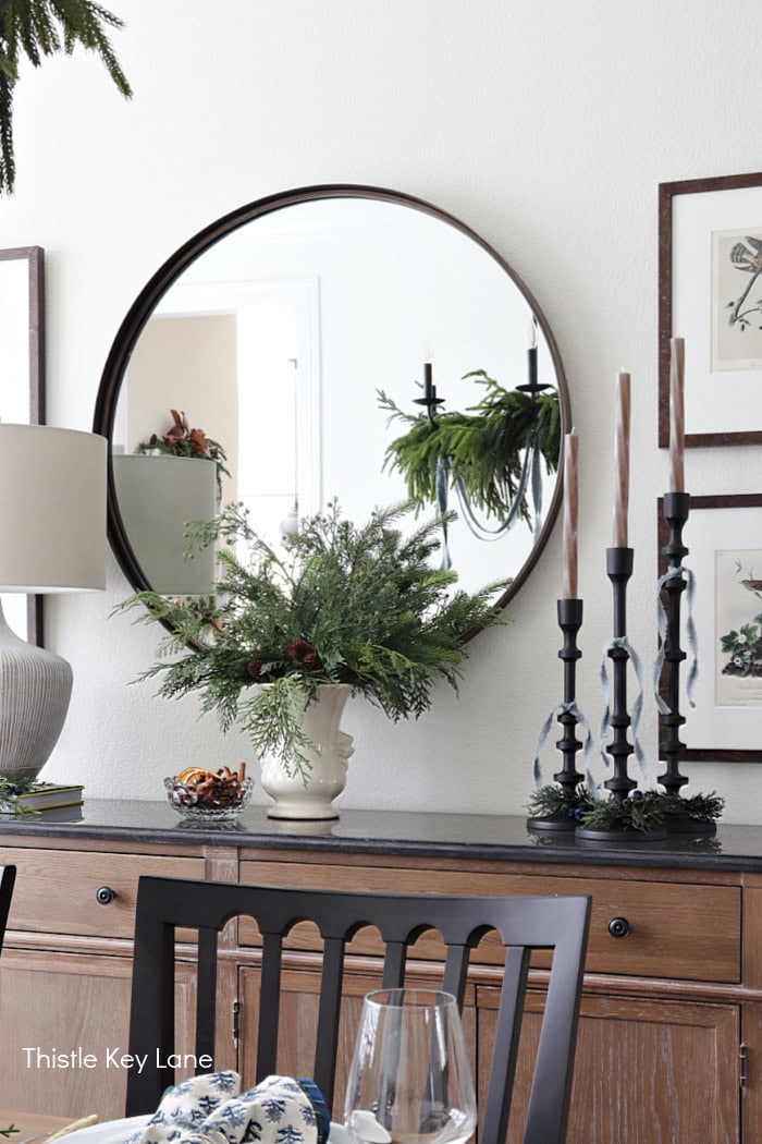 Mirror over buffet with large arrangement. Holiday Dining Room With Festive Greenery.