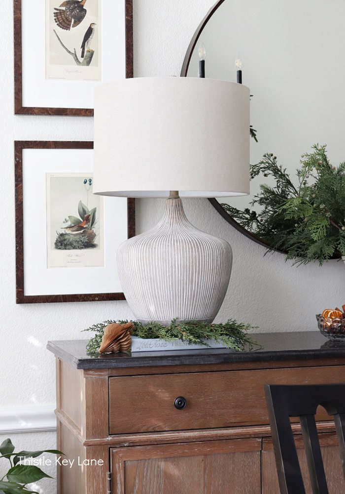 Lamp on a book with artwork and mirror. Holiday Dining Room With Festive Greenery.
