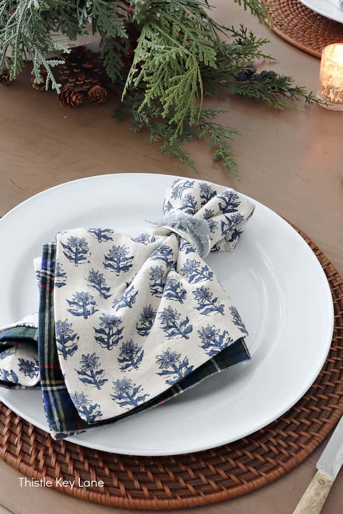Block print blue flower napkins on a white plate. Holiday Dining Room With Festive Greenery.
