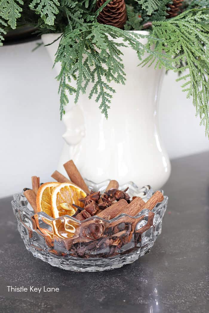 Vintage glass bowl with orange slices and cinnamon sticks. Holiday Dining Room With Festive Greenery.