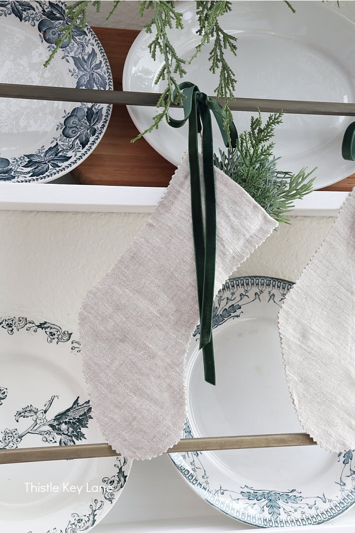 Linen stocking with green ribbon tied to a plate rail. How To Decorate With Homemade Stockings.