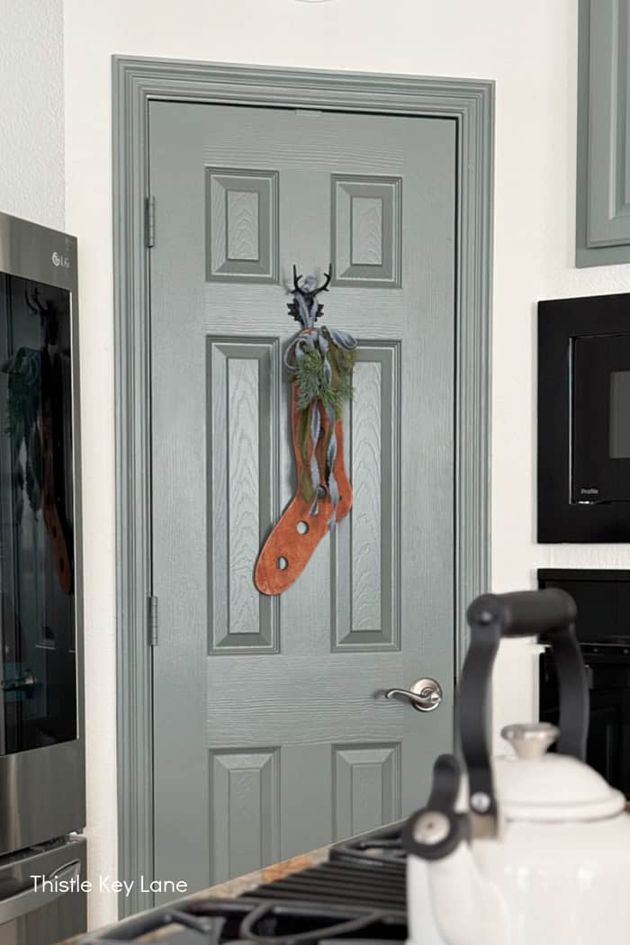 Wood stocking stretcher with ribbon and greenery on a door.