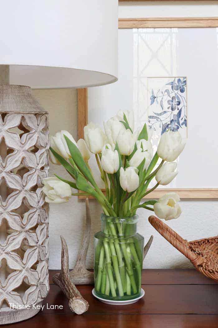 White tulips in a vintage glass jar, deer shed and lamp. How To Create A Garden Basket Vignette.