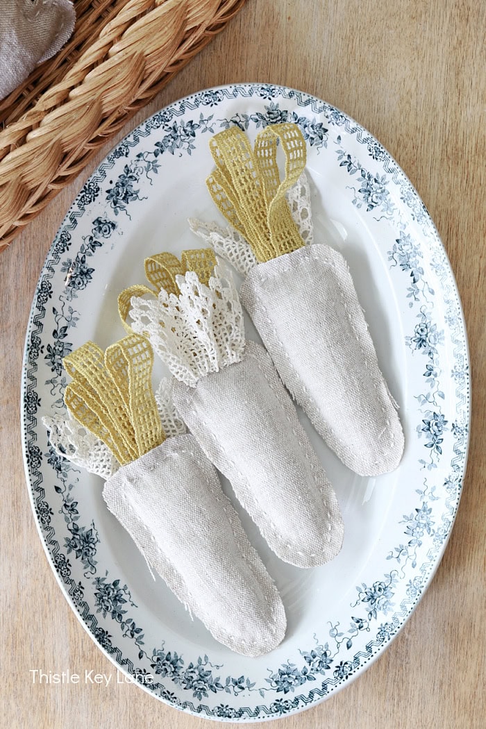 Fabric carrots with lace on a oval platter. DIY Lace Bunny And Carrot Pillows.