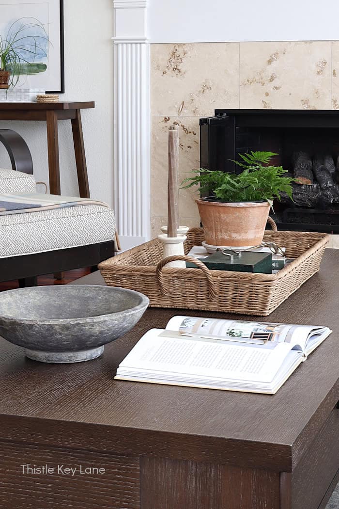 Coffee table with large bowl, open book and wicker tray.