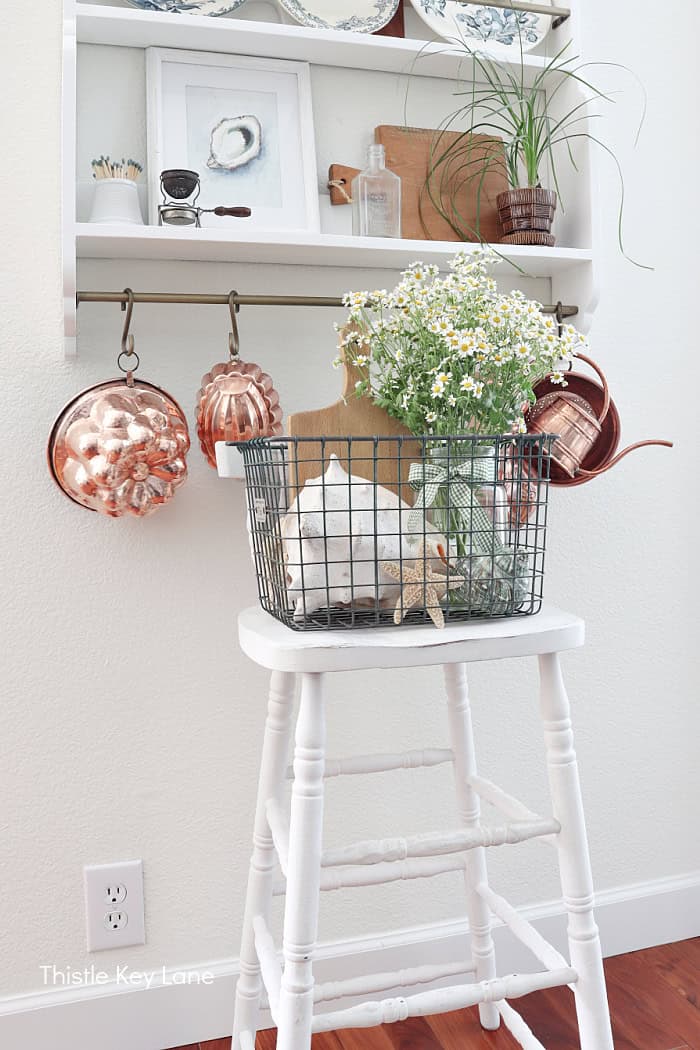 White counter stool with a basket of shells and flowers. How To Decorate With A Wire Basket.