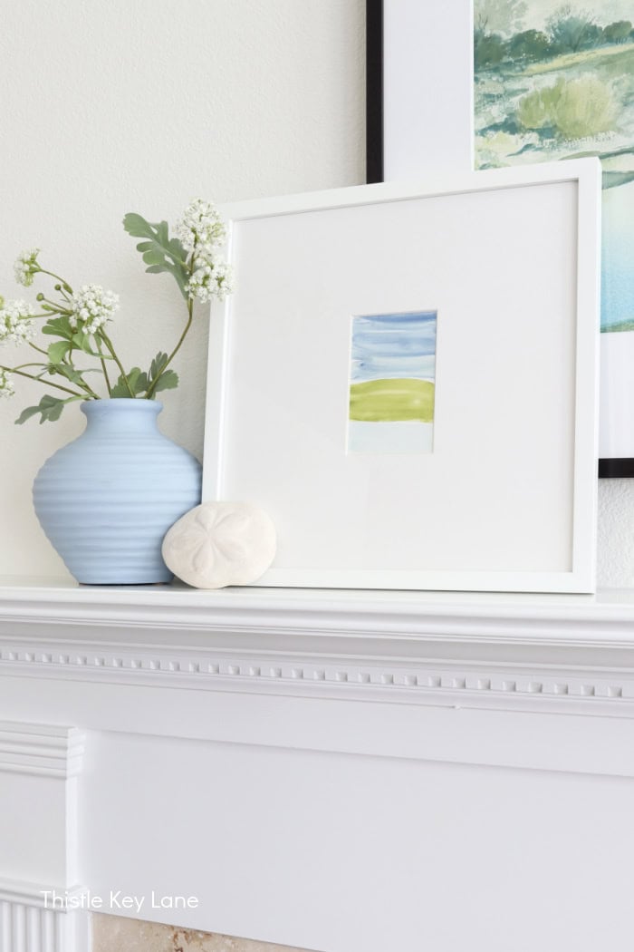 Blue vase and coastal artwork on mantel.