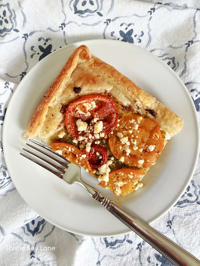 Sliced tart on a plate with a fork. Tomato Pesto Puff Pastry Tart.