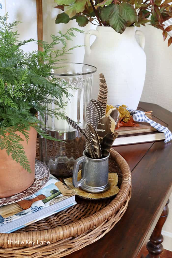 Layering accessories on a wicker tray for fall. Early Fall Entry Table With Greenery.