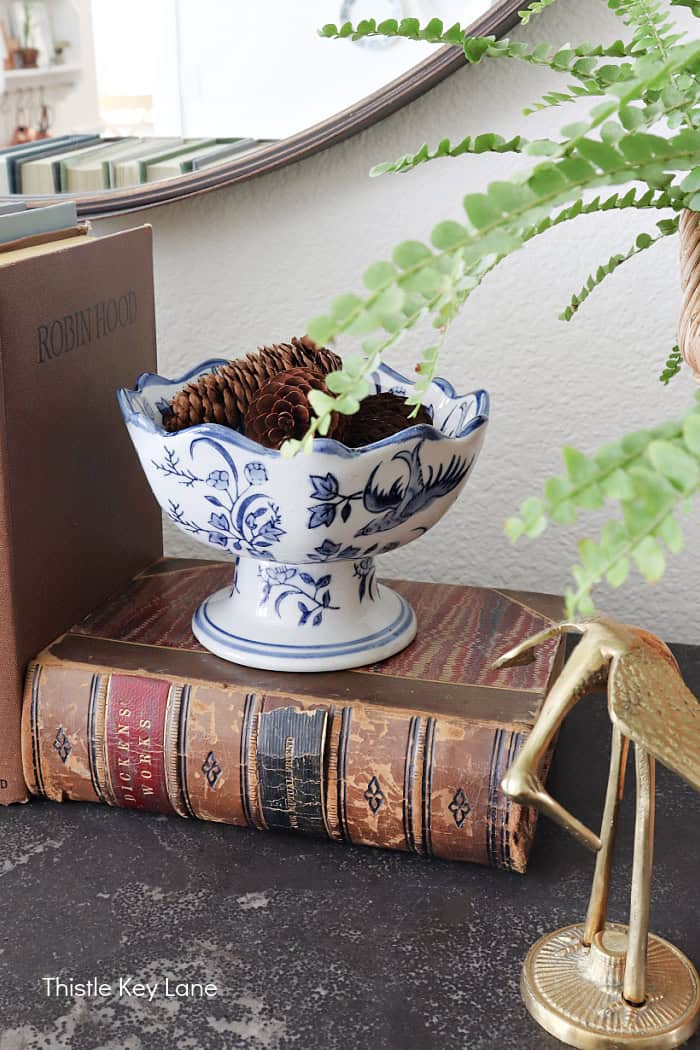 Footed blue and white bowl holding pinecones. Summer To Fall Sideboard Styling.