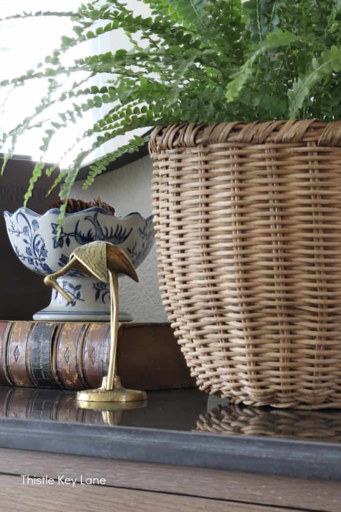 Brass heron, books and a wicker basket holding a plant. Summer To Fall Sideboard Styling.