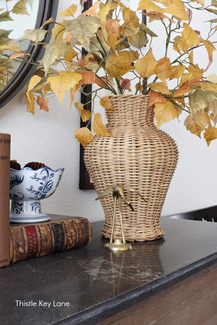 Wicker vase holding fall stems with yellow leaves. Summer To Fall Sideboard Styling.