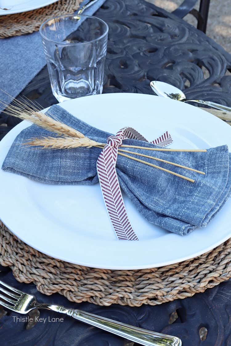 Blue cloth napkins with ribbon and wheat stocks. Charming Rustic Fall Al Fresco Tablescape Ideas.